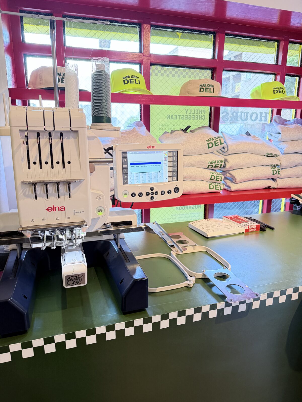 Merch Troop embroidery machine set up at an event with finished caps on the shelf behind it